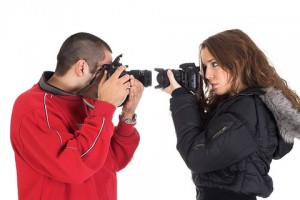 Un chico y una chica ambos con cámara en mano, dirigen sus objetivos uno hacia el otro, llevando el objetivo al rostro de cada uno respectivamente