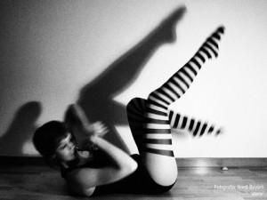 Hedy en una fotografía en Blanco y Negro, vestida con una malla negra y una medias de rayas estirada en un suelo de madera moviendo las piernas